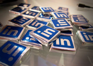 Scattered chocolates, wrapped in silver foil labeled with the LinkedIn logo, on a table.